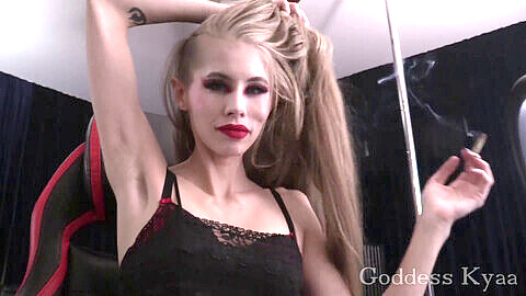 Maîtresse blonde fumeuse taquine en session webcam, avec des tours de fumée et des lèvres rouges